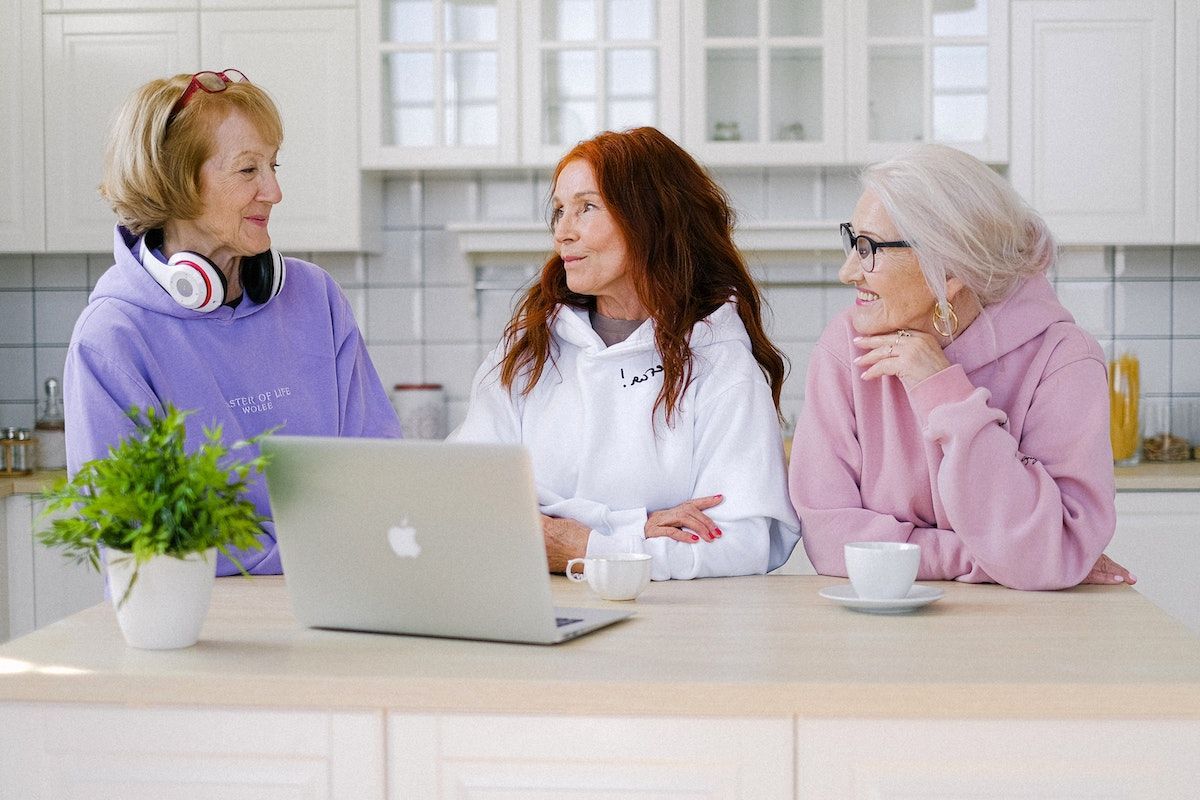 Három idősebb nő vidáman kávézik egy laptop előtt a konyhában