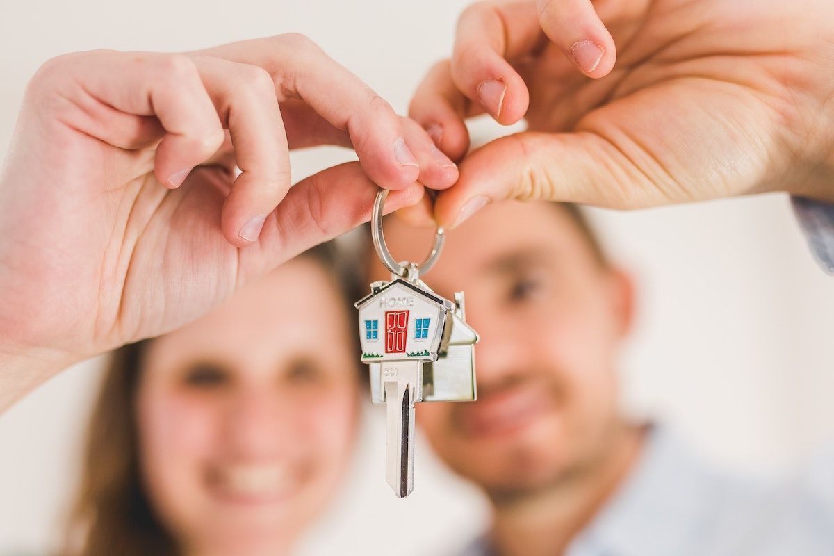 Két mosolygó ember tart egy kulcsot amin egy ház alakú kulcstartó van