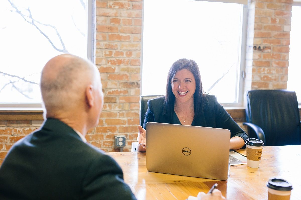 Üzleti tárgyalás, laptop mögött mosolyog az üzlettársra egy nő