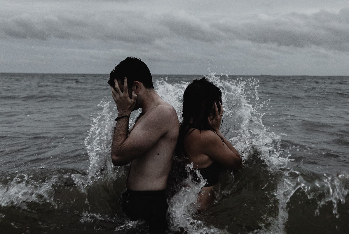 Egy férfi és egy nő fogja a fejét a tengerben egymásnak háttal