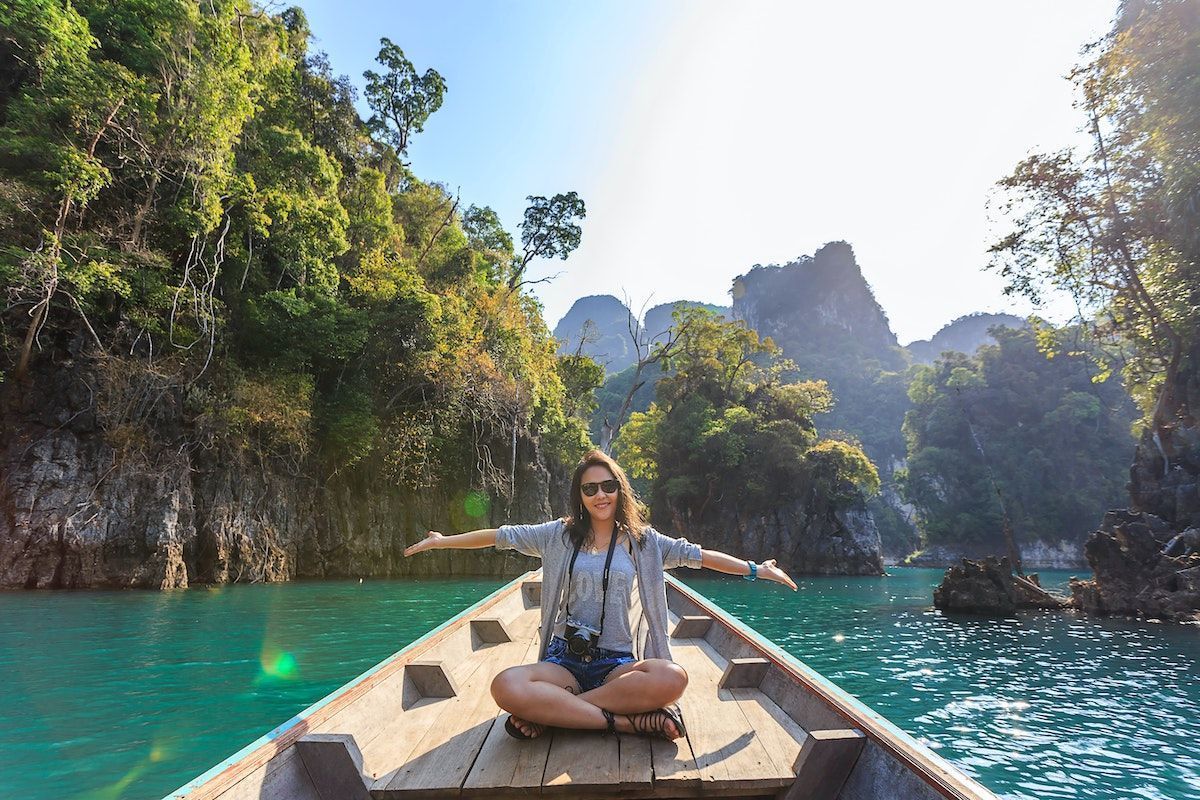 Trópusi környezetben hajón ül egy fiatal nő széttárt karokkal