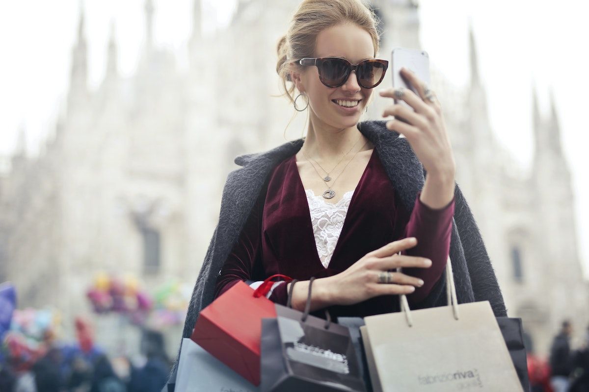 Boldog fiatal nő napszemüvegben nézi a telefonját egy óvárosi főtéren
