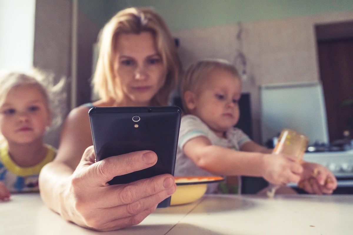 Egy anyuka két kisgyermeke mellett nézi a mobilját